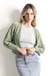 Mujer con cárdigan verde de punto, top corto gris y falda de mezclilla clara.