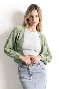 Mujer con cárdigan verde de punto, top corto gris y falda de mezclilla clara.