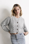 Mujer con cárdigan gris de punto grueso y pantalón de mezclilla claro, moda femenina.