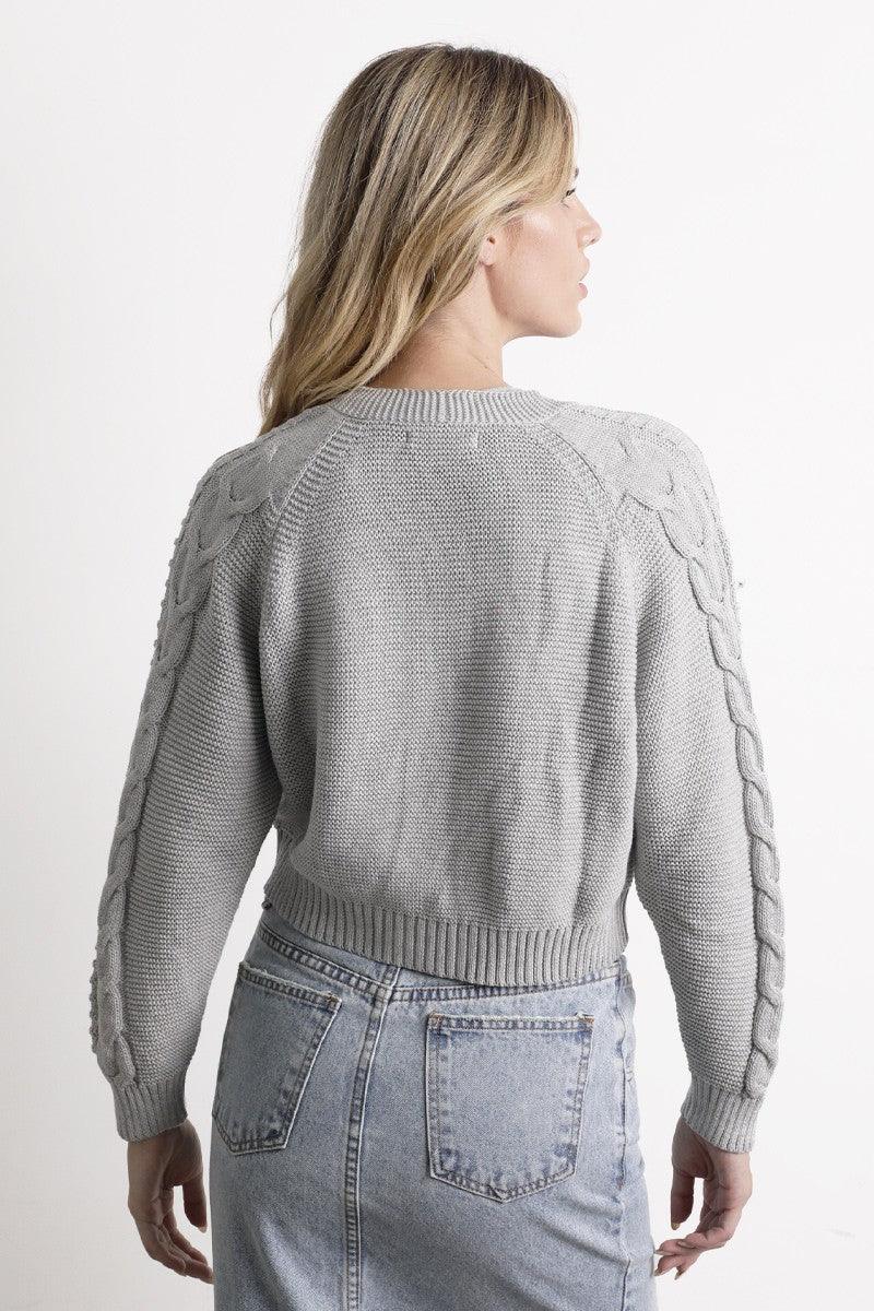 Mujer con suéter gris tejido y falda de mezclilla clara, vista de espaldas, moda femenina casual
