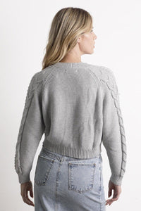 Mujer con suéter gris tejido y falda de mezclilla clara, vista de espaldas, moda femenina casual