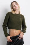 Mujer con top tejido verde olivo manga larga, falda negra y look casual moderno